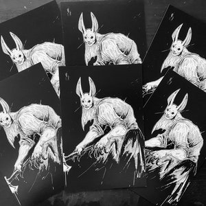 May include: A collection of rectangular art prints featuring a black and white illustration of a humanoid figure with long rabbit ears and a mask, wearing a shirt and pants, holding an axe with both hands in a dynamic, forward-leaning pose.