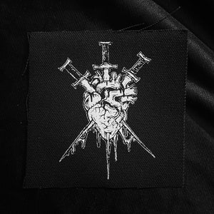 Pode incluir: Patch bordado em preto e branco que representa um coração atravessado por três espadas. O coração está pingando sangue e as espadas têm detalhes intrincados.