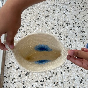 May include: A white crocheted bag with two blue flower designs on the inside.