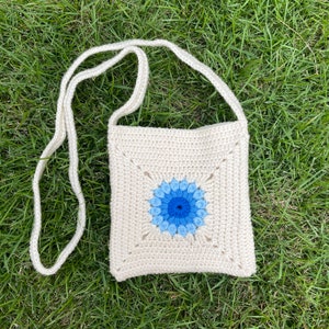 May include: A white crocheted crossbody bag with a blue and light blue flower design.