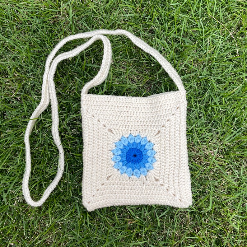 May include: A white crocheted crossbody bag with a blue and light blue flower design.