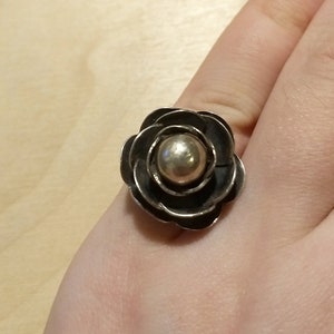 May include: A silver ring with a black flower design and a gold center.