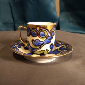 May include: A white porcelain teacup and saucer set with a gold rim and blue and green floral pattern.