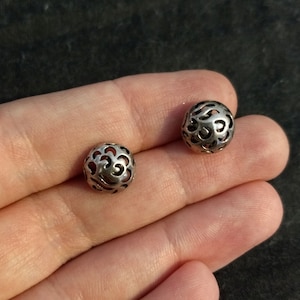 May include: Two silver filigree ball beads with a delicate, intricate design. The beads are round and have a hollow center.