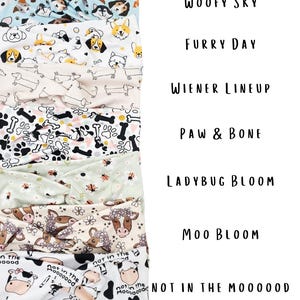 May include: A stack of fabric headbands with various patterns. Designs include dogs, bones, ladybugs, and cows. Text on the image reads "Woofy Sky", "Furry Day", "Wiener Lineup", "Paw & Bone", "Ladybug Bloom", "Moo Bloom", and "Not in the Mooood".