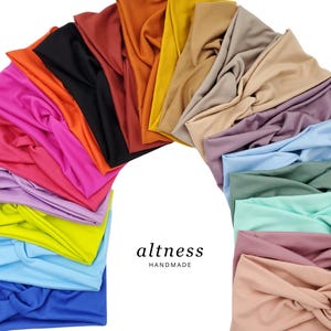 May include: A collection of 15 colorful, stretchy, knotted headbands in various colors, including black, orange, yellow, brown, purple, blue, green, pink, and red. The headbands are arranged in a semi-circle shape. The text "altness HANDMADE" is visible in the center of the image.