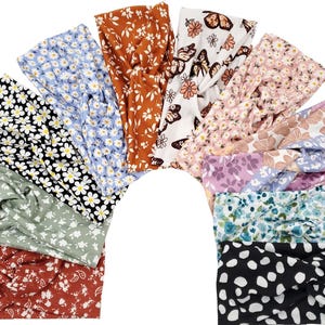 May include: A collection of ten fabric headbands arranged in a fan shape, featuring various patterns including floral prints in blue, white, black, green, and rust, as well as butterfly motifs and black and white polka dots, each with a central twist.