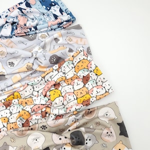 May include: Four colorful headbands with cat patterns. The headbands feature various designs, including cats, fish bones, and paw prints. The colors include blue, gray, white, orange, and tan. These headbands are a fun accessory.