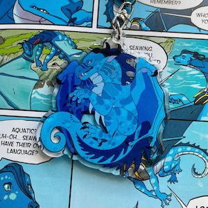 May include: A blue and black dragon character charm with a white background. The charm is attached to a silver key chain. The dragon is in a curled up position with its wings spread out. The text "SEAWING" is visible on the charm.