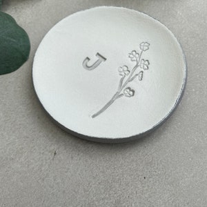 May include: White ceramic ring dish with a floral design and the letter "J" embossed on the surface.