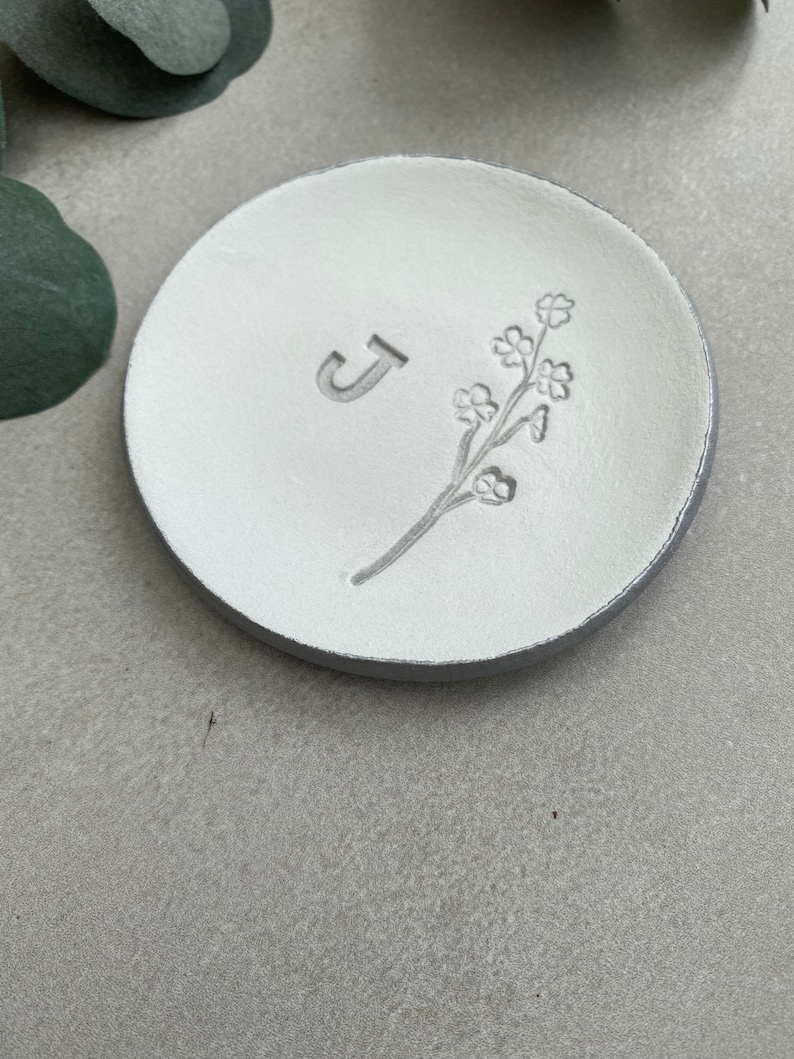May include: White ceramic ring dish with a floral design and the letter "J" embossed on the surface.
