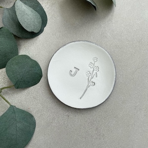 May include: White ceramic ring dish with a floral design and the letter "J" embossed on the surface.