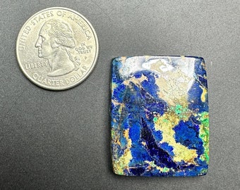 May include: A blue, green, and gold gemstone cabochon with a rectangular shape. The gemstone is about the size of a US quarter.