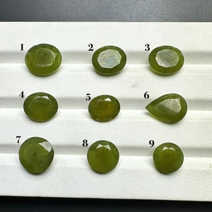 Op de afbeelding: Negen groene edelstenen in verschillende vormen en maten worden gepresenteerd op een wit dienblad. De edelstenen zijn genummerd van 1 tot en met 9.