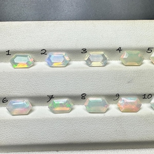 May include: Ten faceted, hexagonal opals are displayed on a white surface. Each opal has a unique play of color, with flashes of green, yellow, pink, and blue. The opals are numbered from 1 to 10.