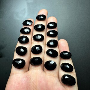 May include: A collection of 15 black oval-shaped gemstones with faceted edges.