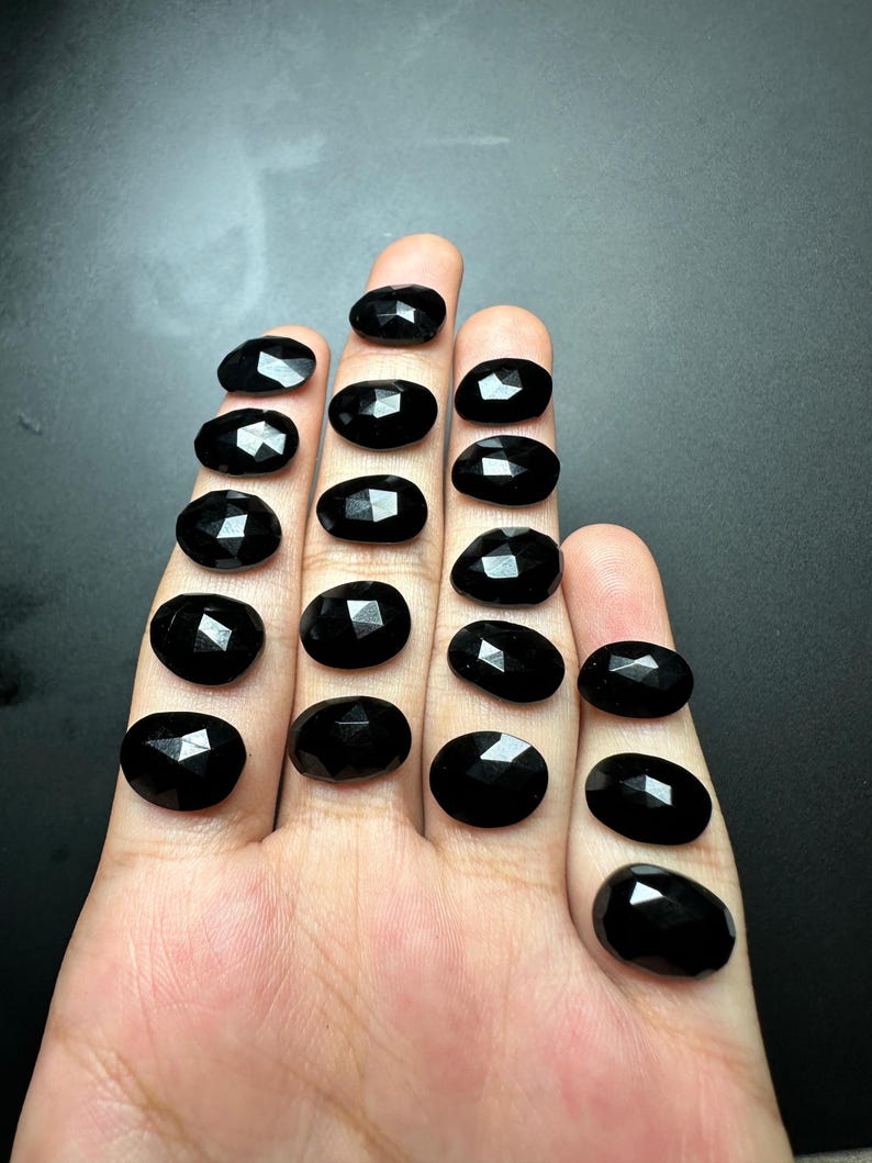 May include: A collection of 15 black oval-shaped gemstones with faceted edges.