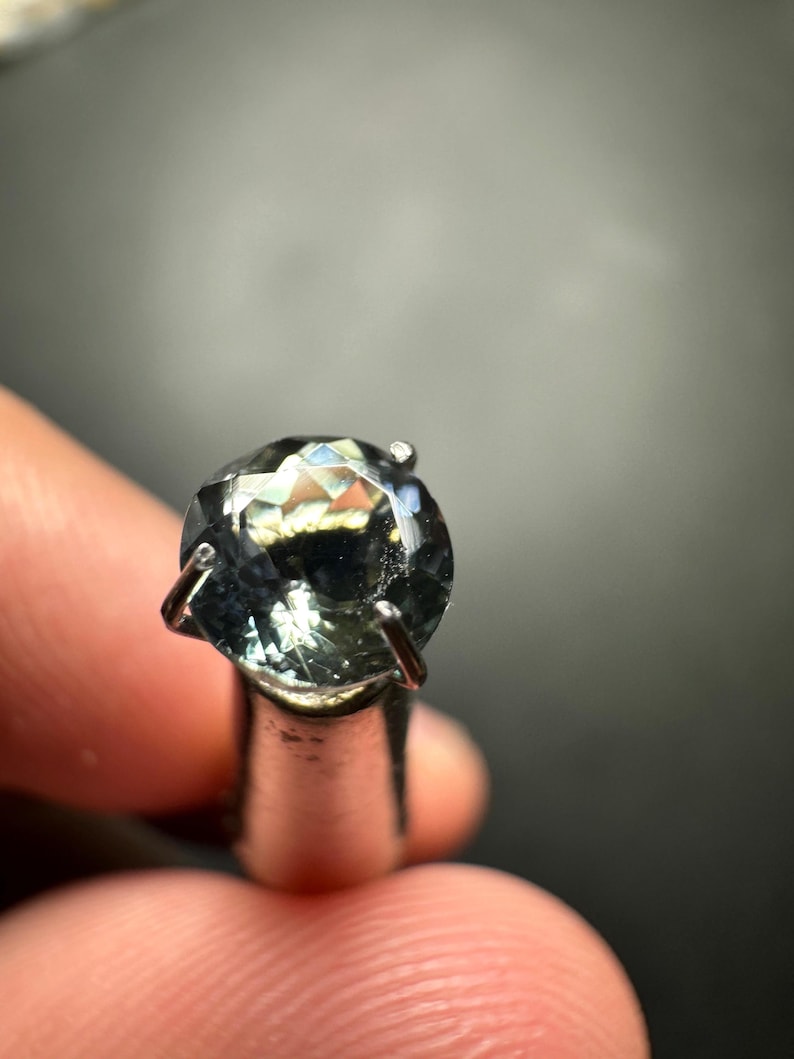 May include: A round, faceted, light blue gemstone with a silver setting.