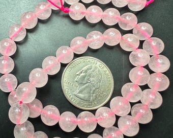 Può includere: Due fili di perline di quarzo rosa, ciascuna di circa 0,8 cm di diametro, infilate su un cordoncino rosa. Una moneta da un quarto di dollaro USA è posta accanto alle perline per il confronto delle dimensioni. Le perline hanno una tonalità rosa traslucida.
