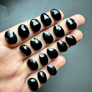May include: A collection of 15 black faceted oval gemstones. The stones are arranged in rows on a hand.