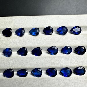 May include: A collection of 15 pear-shaped blue gemstones arranged in three rows of five. The gemstones are displayed on a white surface.
