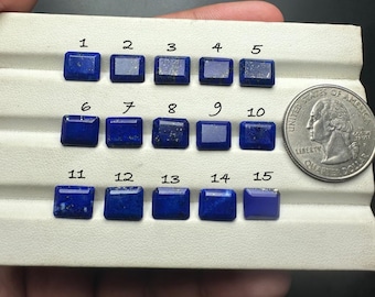 May include: Fifteen square-cut, deep blue lapis lazuli gemstones are displayed on a white surface, next to a quarter coin for size comparison. The gemstones vary slightly in color and texture.