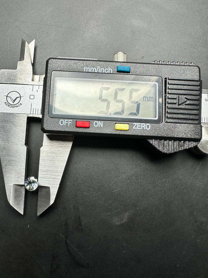May include: A close-up of a digital caliper measuring a small, light blue gemstone. The caliper reads 5.5 mm.
