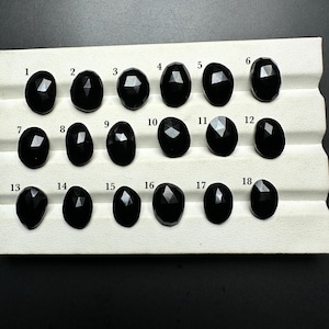 May include: A set of 18 black gemstones, numbered 1 through 18, arranged in rows on a white surface. The gemstones are faceted and have a shiny, polished finish.