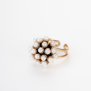 Anello artigianale dorato a cupola con cluster di perle bianche su fondo chiaro.
