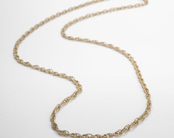 May include: A gold-colored necklace with a rope chain design. The necklace is displayed on a white background. The chain is made of small, interconnected links, creating a textured appearance. The necklace is a classic jewelry piece.