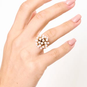 Anello fascia dorata con cupola di perle indossato sulla mano con smalto rosa.