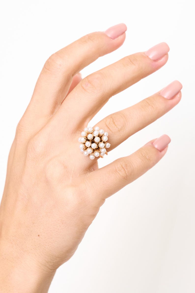 Anello fascia dorata con cupola di perle indossato sulla mano con smalto rosa.