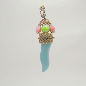 May include: A pendant featuring a light blue horn-shaped charm. The pendant has a gold-colored filigree design with pink and green gemstones. The top has a decorative bail for hanging.