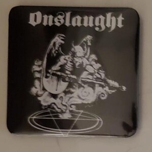 May include: Black square button with the word "Onslaught" in a gothic font. The button features a white illustration of a demonic figure with wings, a halo, and a pentagram.