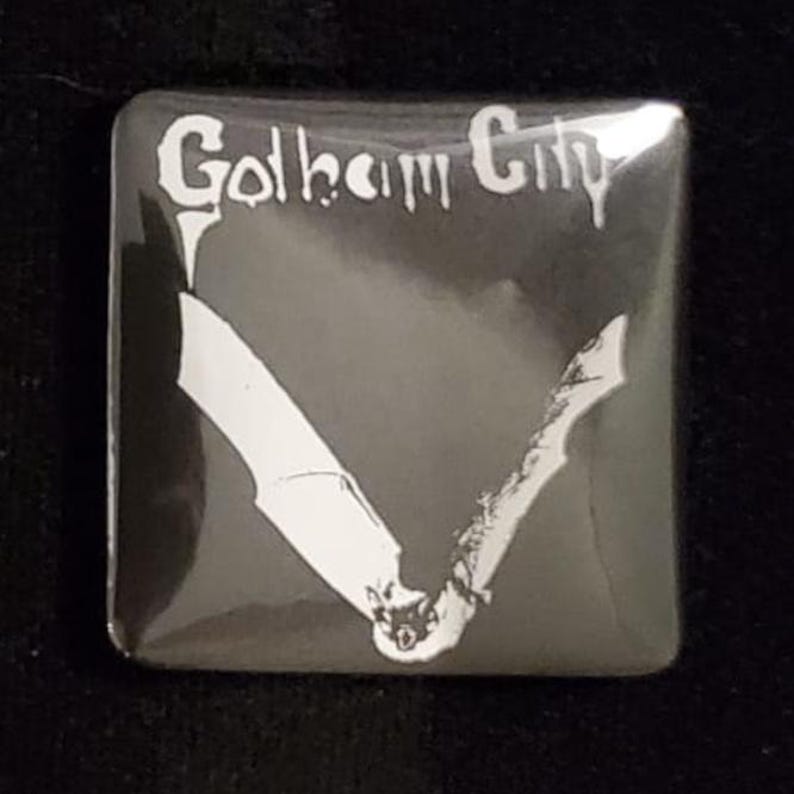 Puede incluir: Bot&oacute;n cuadrado con fondo negro e ilustraci&oacute;n de murci&eacute;lago blanco. El texto "Gotham City" est&aacute; escrito en blanco en la parte superior del bot&oacute;n. El bot&oacute;n es cuadrado con esquinas redondeadas.