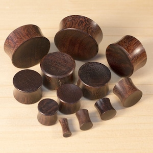 May include: A set of 11 wooden ear gauges in various sizes. The gauges are made of dark brown wood with a natural grain pattern.