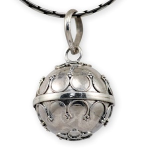 Puede incluir: Un colgante de plata en forma de esfera con un diseño decorativo. El colgante está unido a una cadena negra.