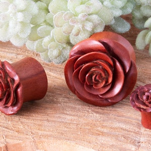 May include: Three wooden rose plugs in various sizes. The plugs are carved with a detailed rose design and are a reddish-brown colour.
