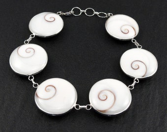 May include: A silver bracelet with six white shell charms featuring a brown spiral pattern. The bracelet has a lobster clasp closure.