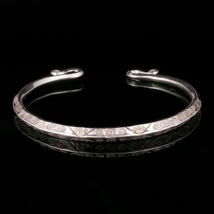 以下が含まれることがあります： 幾何学模様のシルバーバングルブレスレット。ブレスレットは滑らかで磨かれた仕上げで、手首に快適にフィットするように設計されています。