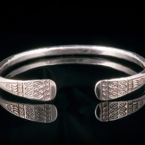 Könnte beinhalten: Ein silbernes Armreif-Armband mit gehämmerter Oberfläche und komplizierten geometrischen Mustern an den Enden.