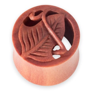 May include: A round wooden ear gauge with a carved leaf design. The gauge is a reddish-brown colour.
