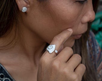 May include: A silver ring featuring a triangular-shaped white and grey spiral shell inlay, paired with matching stud earrings. The jewelry set showcases a polished metallic finish and a distinct natural spiral pattern on each piece of the set.