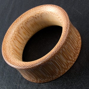 Könnte beinhalten: Ein natürlicher Holz-Ohrenstecker mit einer glatten, abgerundeten Oberfläche. Der Stecker ist aus Bambus und hat eine hellbraune Farbe.