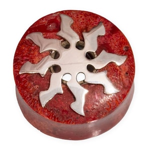 Può includere: Un bottone rotondo in corallo rosso con un design a stella argentata. La stella ha un design a taglio ed è incassata nel corallo.