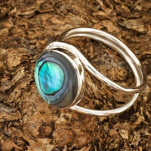 Puede incluir: Un anillo de plata con una incrustación redonda de nácar de abulón. El anillo tiene un diseño simple y elegante, perfecto para el uso diario.