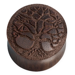 May include: A dark brown wooden ear gauge with a carved tree of life design.