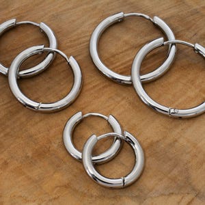 Könnte beinhalten: Vier Paar silberne Creolen in verschiedenen Größen. Die Ohrringe sind aus Metall und haben eine glänzende Oberfläche.