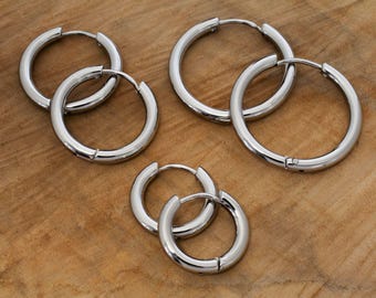 May include: Three pairs of polished silver-tone hoop earrings in varying sizes. Each pair features a circular design with a hinged closure mechanism, showcasing a smooth, reflective metallic finish across all six individual hoop components.