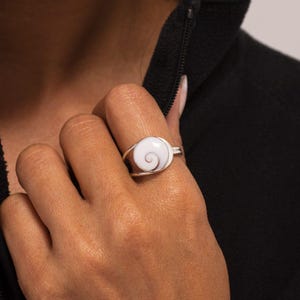 Könnte beinhalten: Ein silberner Ring mit einer weißen und rosafarbenen Muscheleinlage mit einem Spiraldesign.